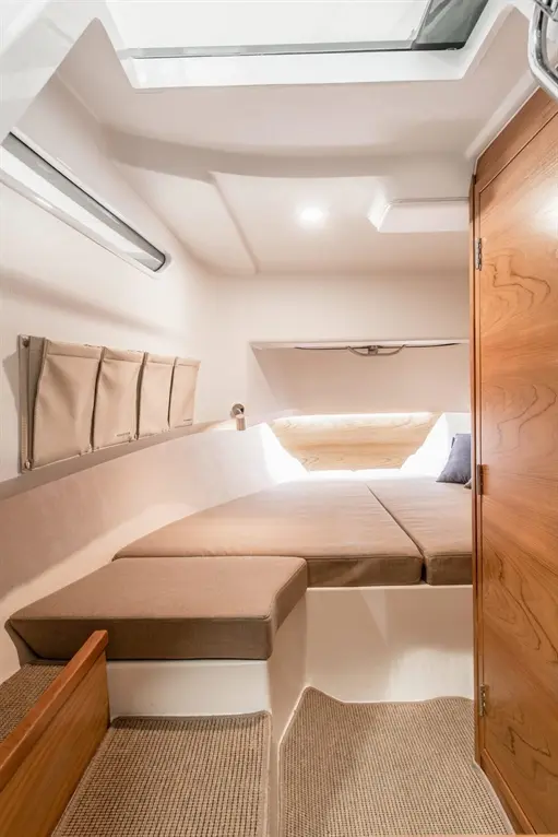 Interior view of a minimalist boat cabin featuring two cushioned beds, a storage wall organizer, and wooden door, illuminated by natural light.
